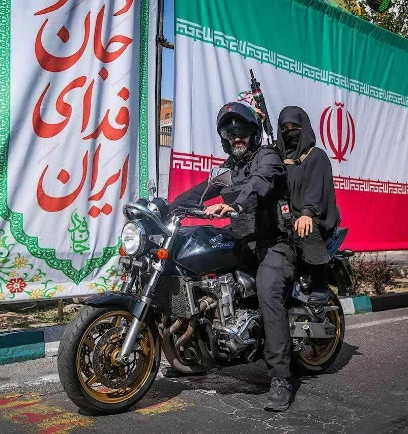 عکس | یک تصویر متفاوت؛ زن سلاح‌بدست روی موتور پشت سر نیروی نظامی در کنار پرچم جمهوری اسلامی ایران